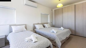 A hotel room with two beds, a wardrobe, and an air conditioning unit.