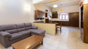A modern kitchen with wooden cabinets, a dining area with a table and chairs, and a grey sofa in a living room.