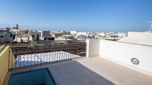 A rooftop terrace with a swimming pool, a view of the cityscape, and a clear sky.