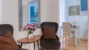 Un salon moderne avec deux fauteuils sombres, une petite table ronde ornée d’un vase de fleurs et un grand miroir accroché au mur.