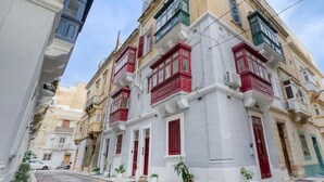 Une rue étroite bordée de bâtiments traditionnels aux façades rouges et blanches, agrémentée de balcons et de petites plantes.