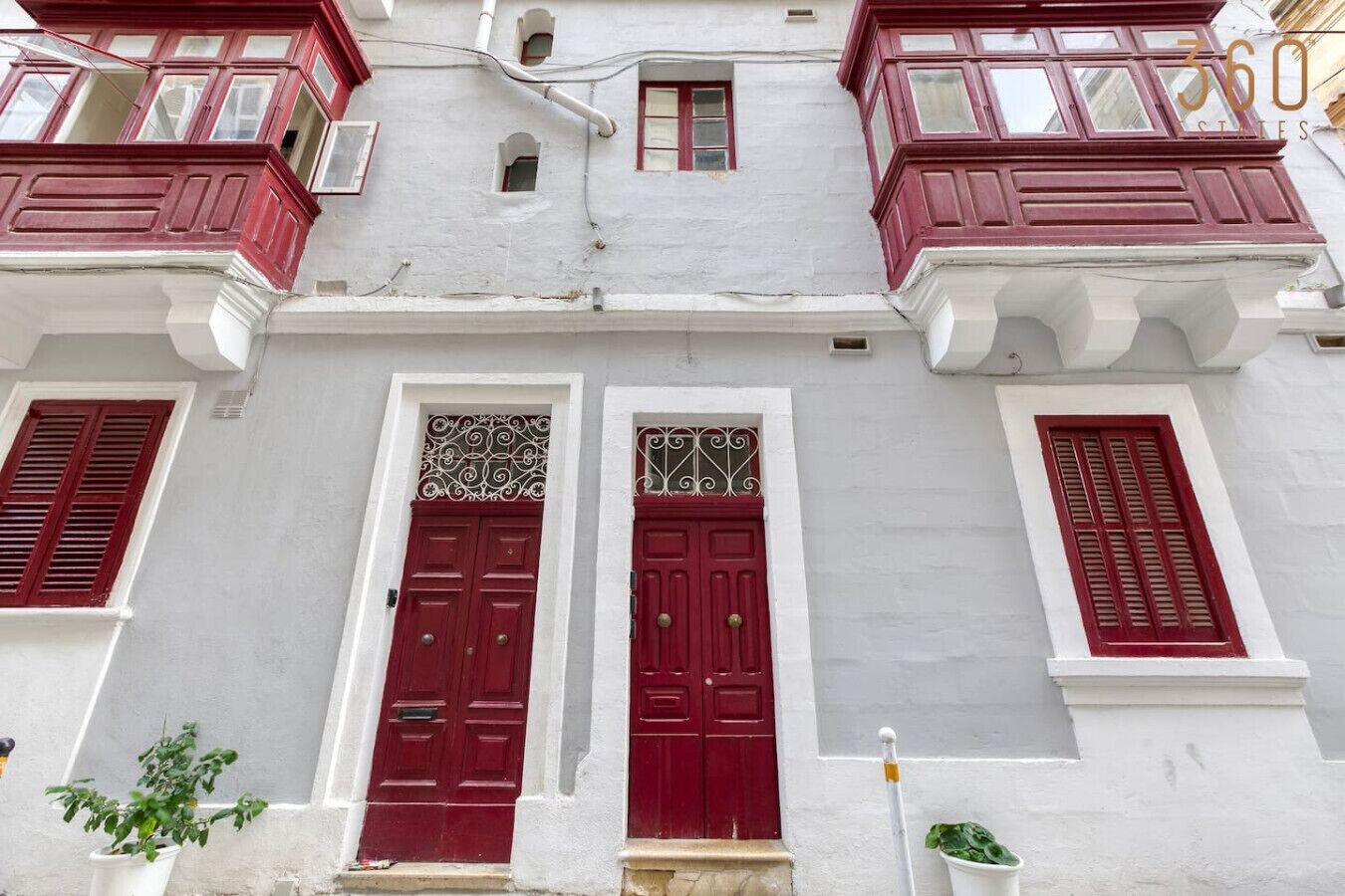 Un edifici amb dues portes vermelles, parets blanques i balcons amb baranes vermelles.