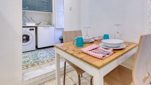 Een kleine keuken met een wasmachine, een eettafel met een blauwe mok en een wijnglas.