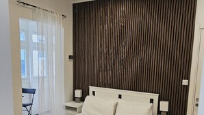 Een slaapkamer met een bed, twee nachtkastjes, een stoel, een raam met gordijnen en een deur.