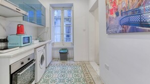 Een kleine keuken met een wasmachine, een magnetron en een rode waterkoker.