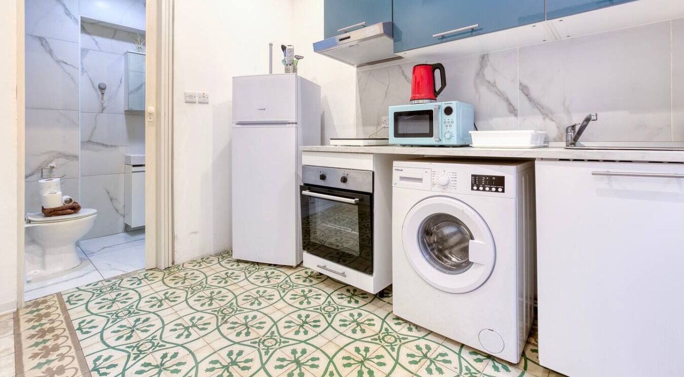 Een kleine keuken met een wasmachine, magnetron, oven en een koelkast.