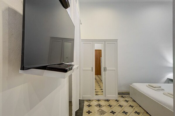 A small, clean room with a TV mounted on the wall, a wardrobe, and a bed.