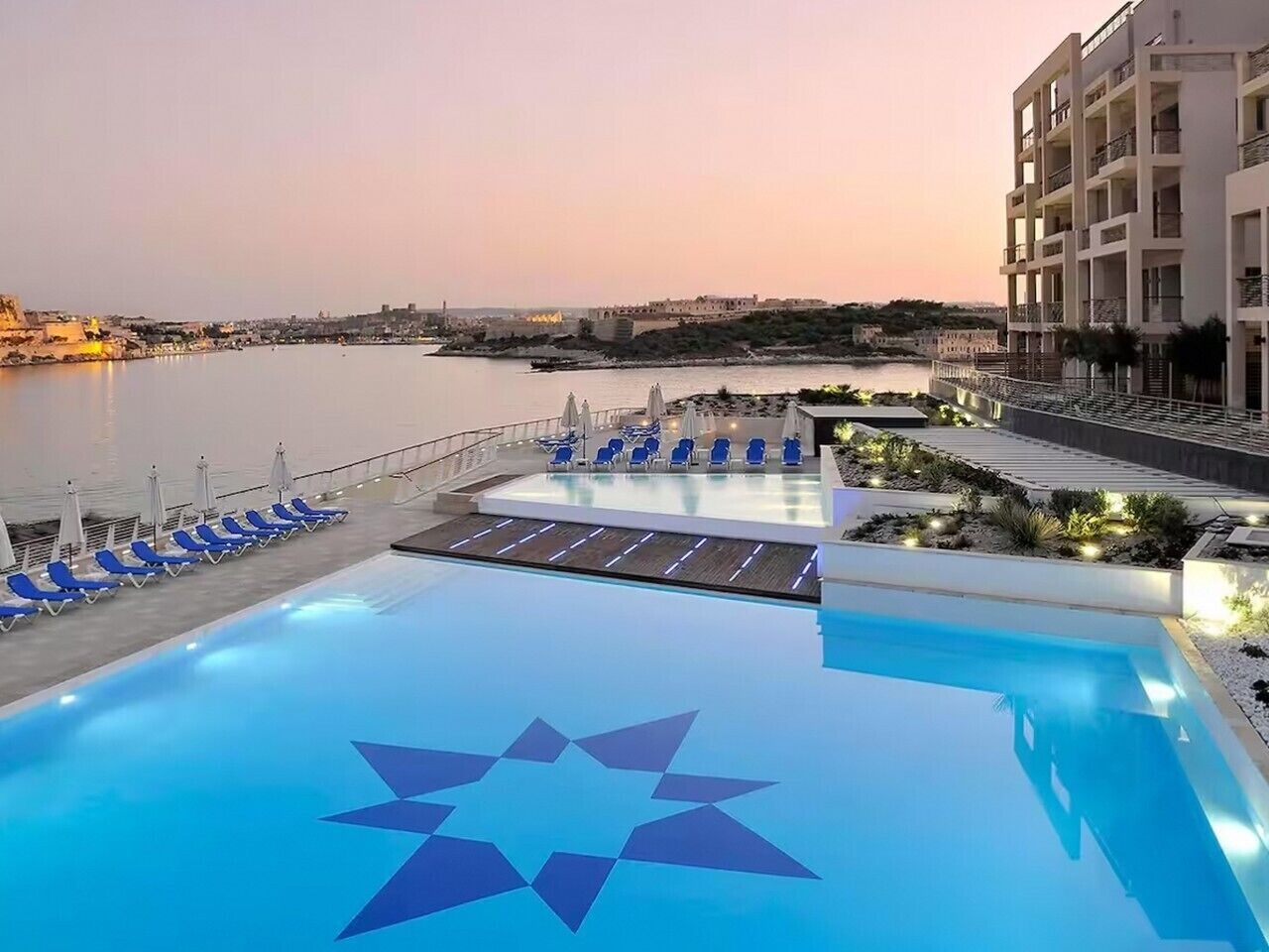 A swimming pool with a star design, lounge chairs, and a view of the sea.