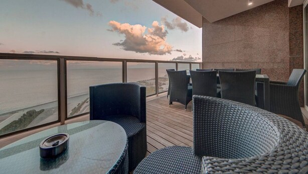 A balcony with wicker furniture, a glass table, and a view of the ocean.
