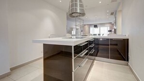 A modern kitchen with a white countertop, stainless steel appliances, and a glass-enclosed pantry.
