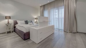 A modern bedroom with a bed, bedside tables, a dresser, and a large window with curtains.