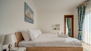 A bedroom with a wooden bed, white bedding, a bedside table with a lamp, a painting on the wall, and a window with curtains.