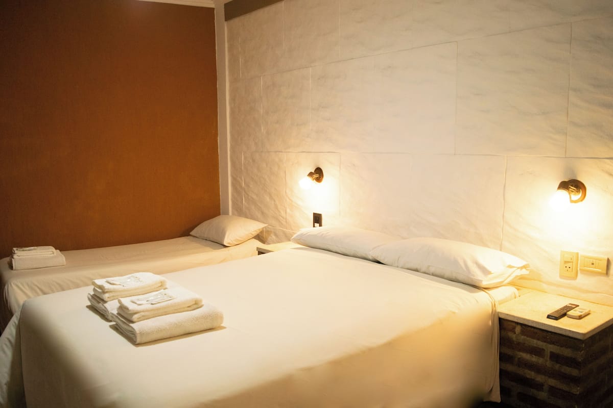 A hotel room with two beds, a nightstand, and a wall-mounted light fixture.
