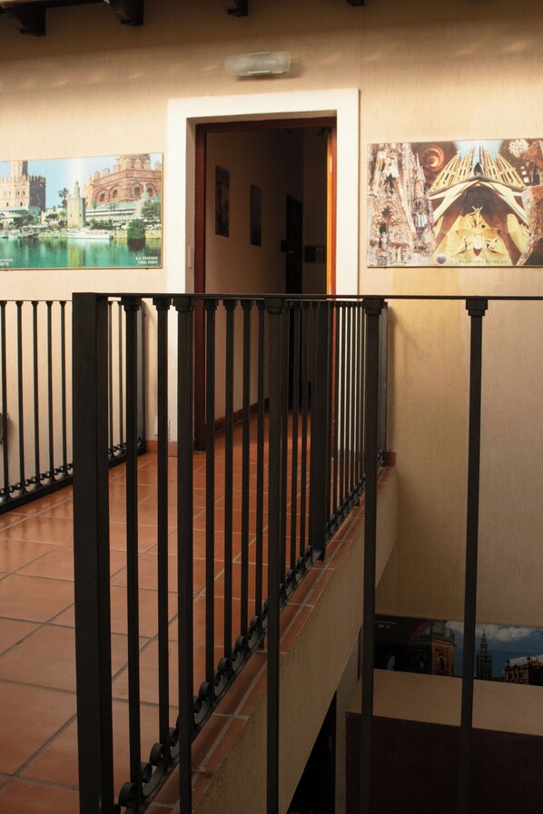 A hallway with a black metal railing, tiled floor, and two framed pictures on the walls. - Hotel del Monumento (Salta)