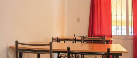 Un comedor con una mesa y sillas de madera, una ventana con cortinas rojas y piso de baldosas.