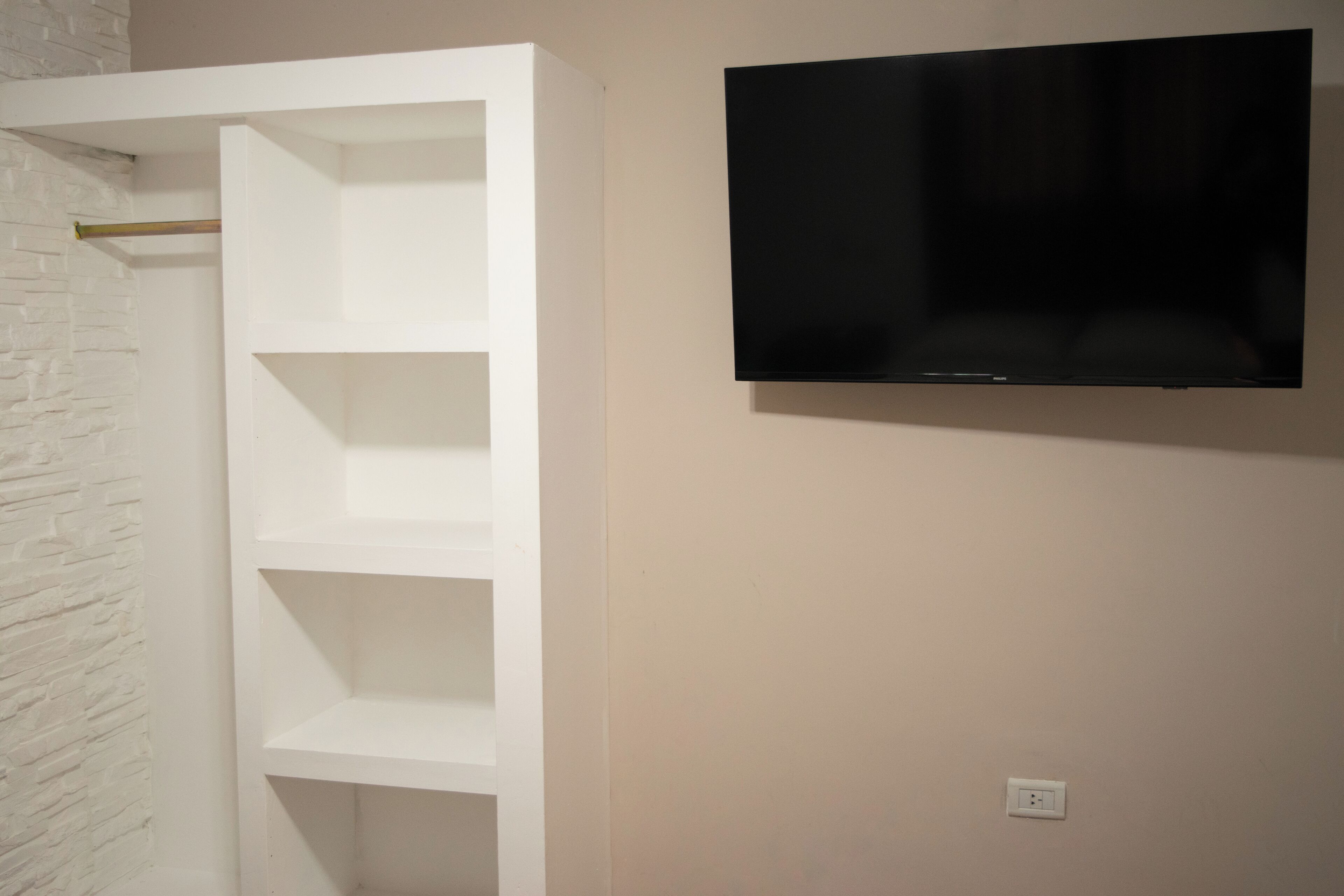 Une étagère blanche à trois niveaux, et un téléviseur à écran plat fixé au mur.