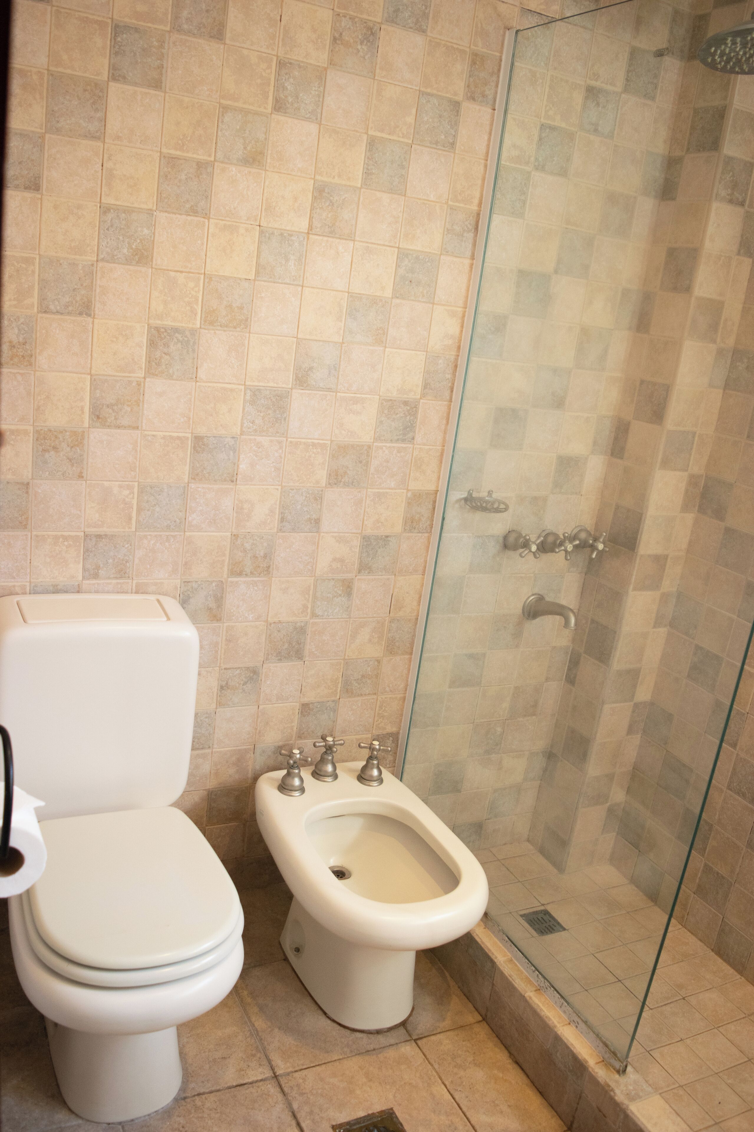 Un baño con inodoro, bidé y ducha con mampara de vidrio.