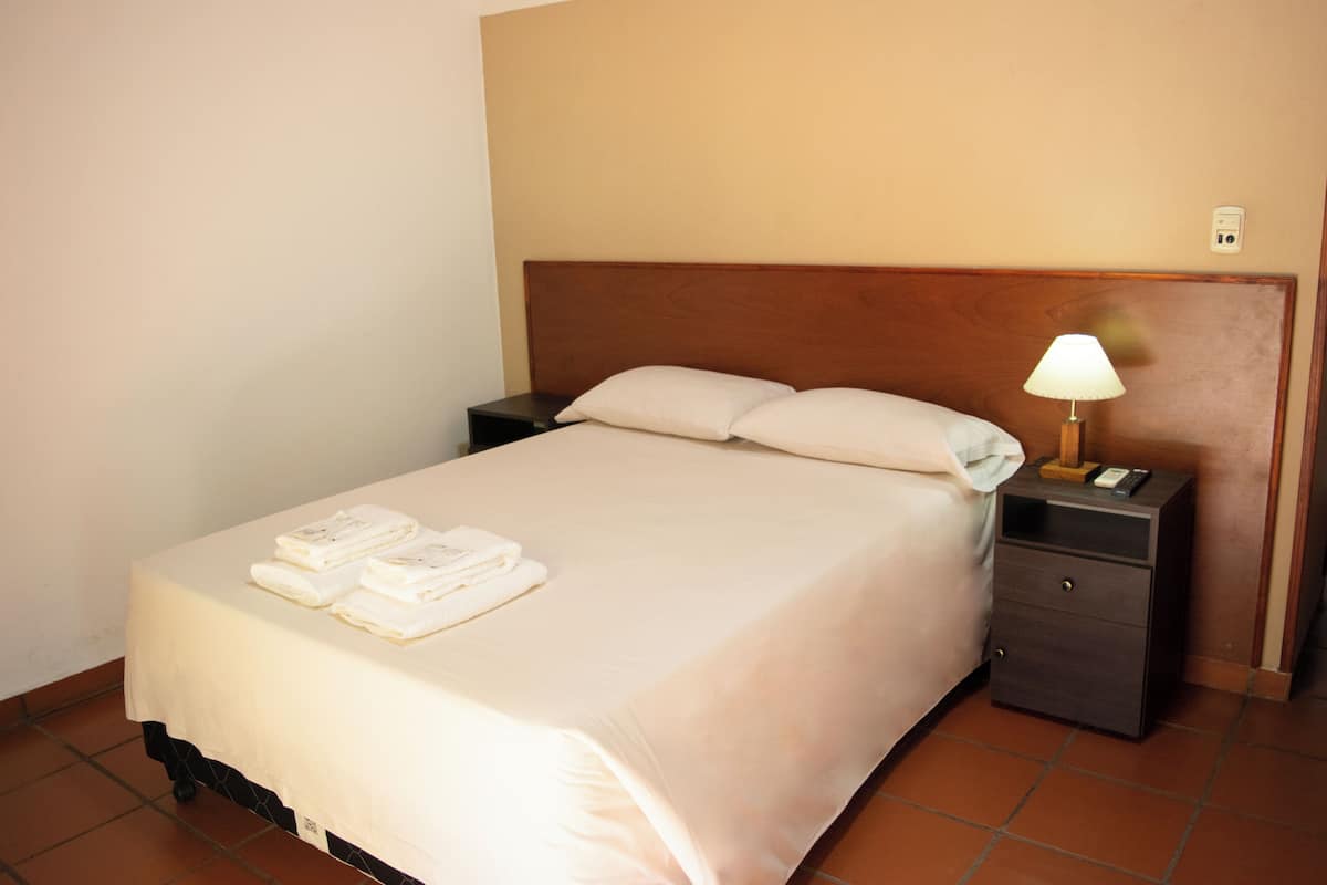 A neatly made bed with white linens and towels, a bedside lamp, and a small wooden nightstand.