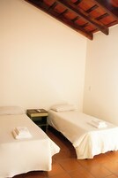 A room with two single beds, a wooden nightstand, and a tiled floor.