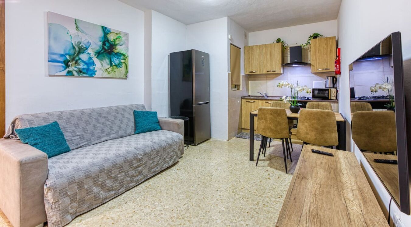 Ein kompakter Wohnraum mit Sofa, Esstisch und Küchenzeile, inklusive Kühlschrank und Mikrowelle.