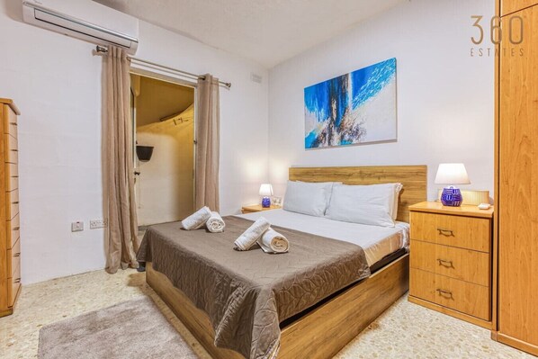 A neatly arranged bedroom with a bed, bedside tables, a wardrobe, and a painting on the wall. - Lovely 1BR Apt with full amenities in Bugibba! (San Pawl il-Baħar)
