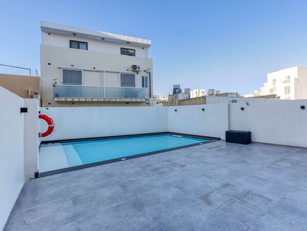Ein Pool auf dem Dach mit einem Rettungsring, umgeben von einem weißen Gebäude mit einem Balkon.