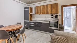 A compact kitchen with modern appliances, a dining area with a wooden table and chairs, and a view of the outside through a glass door.