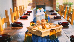 Une longue table à manger entourée de chaises, un plateau en bois avec des oignons et des bouteilles.