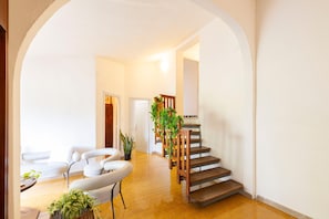 Ein geräumiger Wohnbereich mit einer Holztreppe, weißen Möbeln und Blumentöpfen.