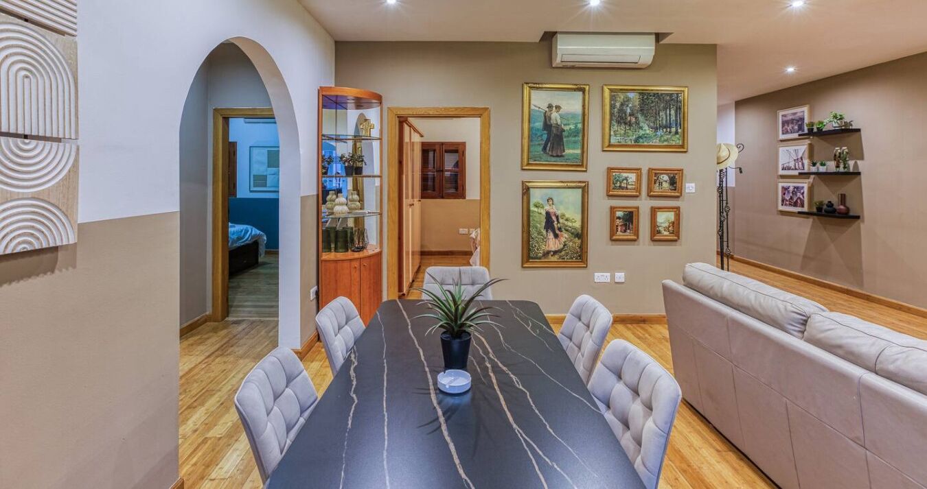Uma área de refeições com uma mesa comprida, cadeiras, um sofá e obras de arte na parede.