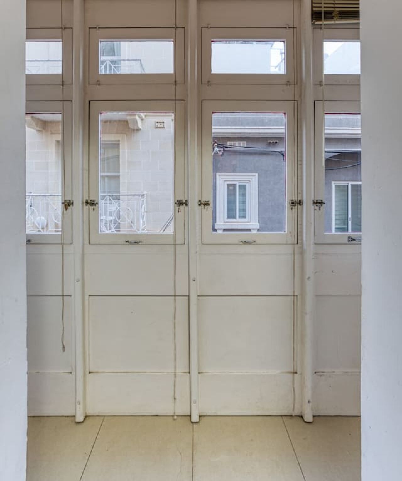 Una hilera de puertas blancas cerradas con pequeñas ventanas que dan a un balcón exterior.