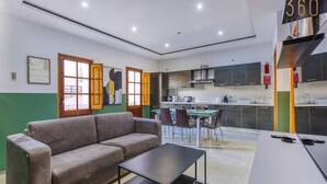 A modern living room with a sofa and coffee table, a dining area with chairs, and a kitchen with a stove and cabinets.