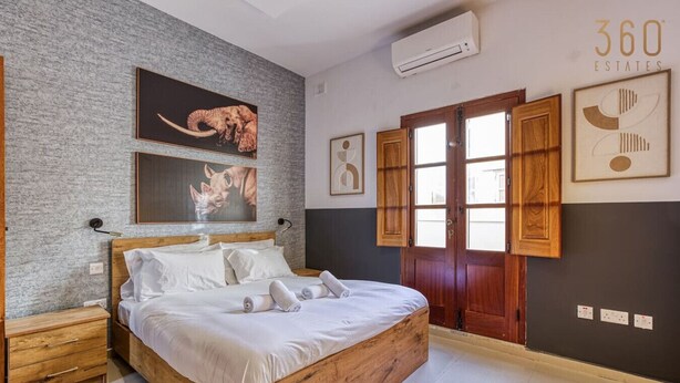 A bedroom with a wooden bed, a grey textured wall, and artwork.