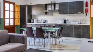 A modern kitchen with a glass dining table, dark cabinetry, and a coffee machine.