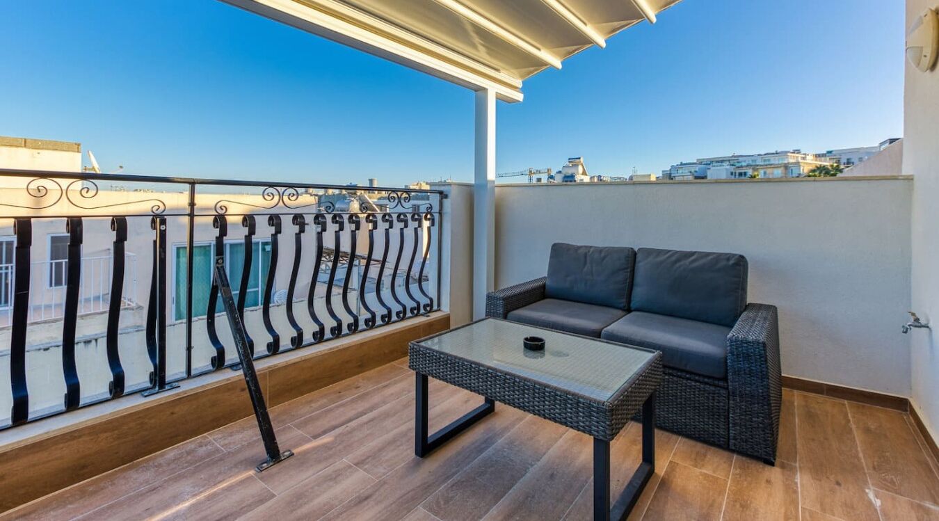 A balcony with a sofa and a table, a railing, and a view of buildings.