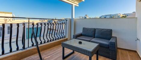 A balcony with a sofa and a table, a railing, and a view of buildings.