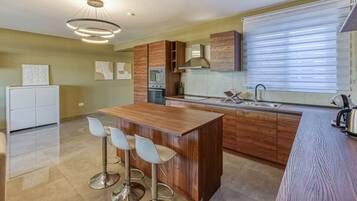 Una cucina moderna con isola centrale, sgabelli da bar, forno integrato e un'ampia finestra con tende.