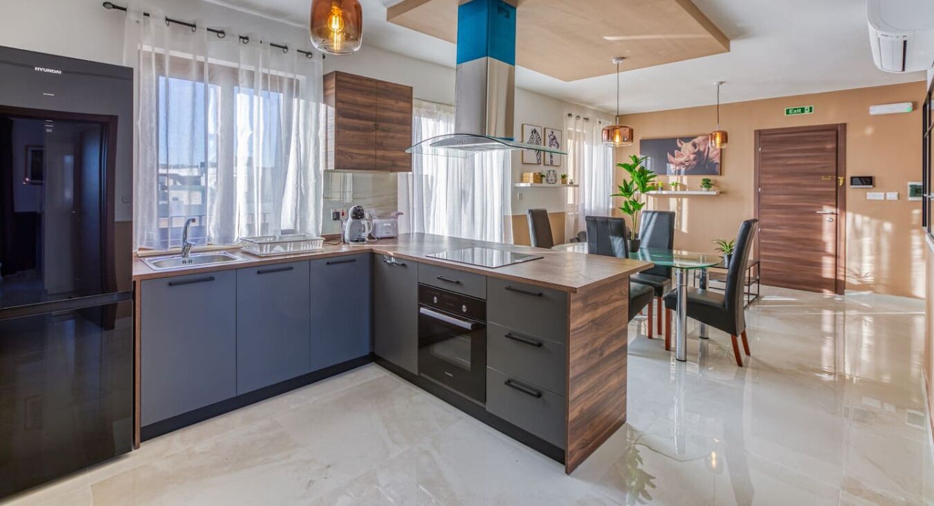 Una cocina moderna con una isla central, electrodomésticos integrados y un comedor con mesa y sillas de vidrio.