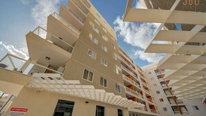 A modern multi-story building with a geometric facade, balconies, and a clear sky. - Brand new, fully equipped 2BR home in Qawra (San Pawl il-Baħar)