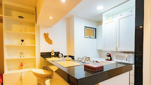 A modern kitchen with a central island, white cabinetry, a microwave, and a coffee maker. - SUH Flamengo 01 Praia Studio Dreams (Rio de Janeiro)