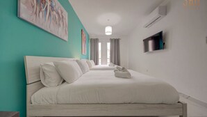 A modern hotel room with a large bed, a flat-screen TV, and artwork on the walls. - Cosy 1BR home with full amenities in central Gzira (Il-Gżira)