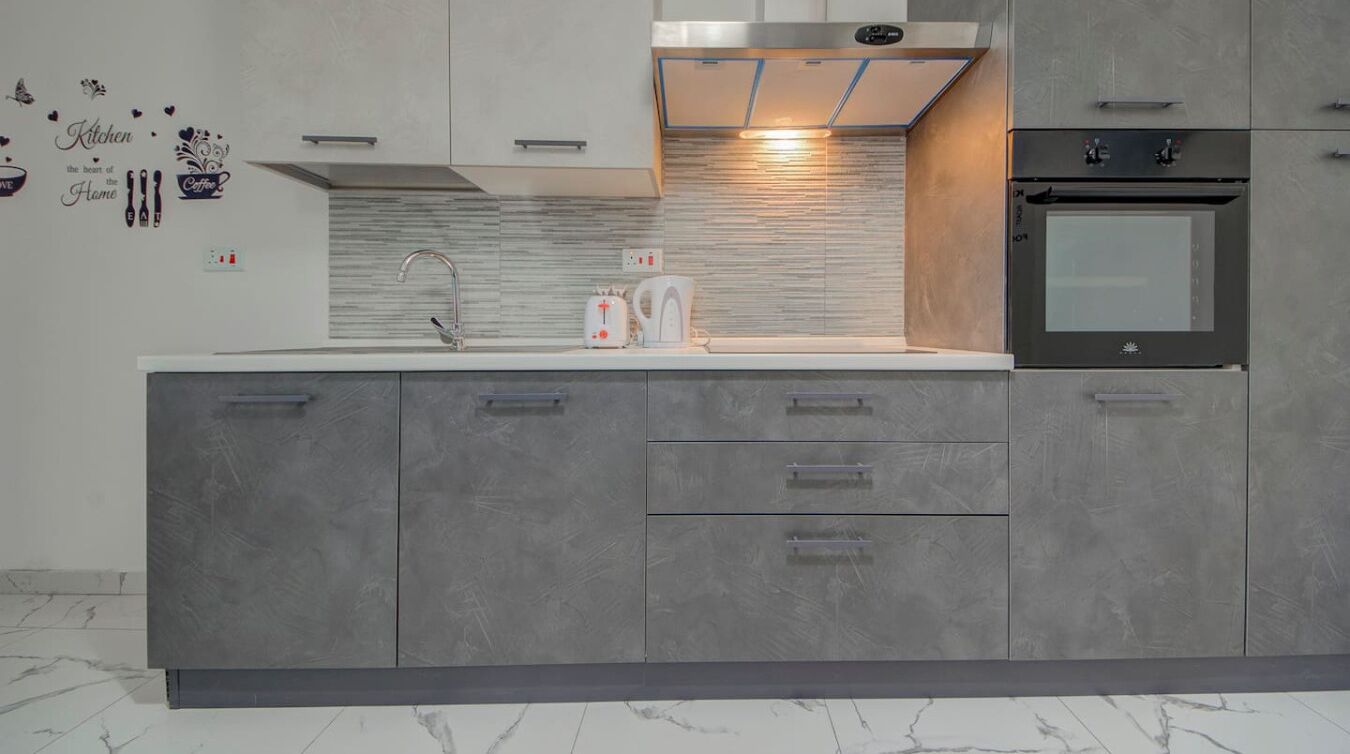 A modern kitchen with grey cabinetry, a stainless steel range hood, a built-in oven, and a marble countertop.