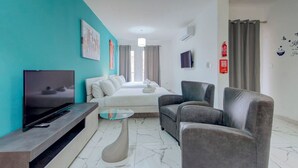 A modern hotel room with a bed, two armchairs, a TV, and a small table. - Cosy 1BR home with full amenities in central Gzira (Il-Gżira)