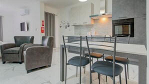 A modern kitchen with a marble countertop, a built-in oven, and a dining area with a glass table and metal chairs. - Cosy 1BR home with full amenities in central Gzira (Il-Gżira)