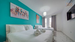 Habitación de hotel con dos camas, una pared de acento color aguamarina, obras de arte y un televisor.