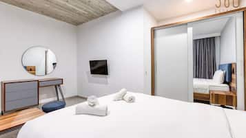Una camera d'albergo moderna con un letto grande, una scrivania, una TV a schermo piatto, uno specchio e una porta scorrevole che conduce al bagno.