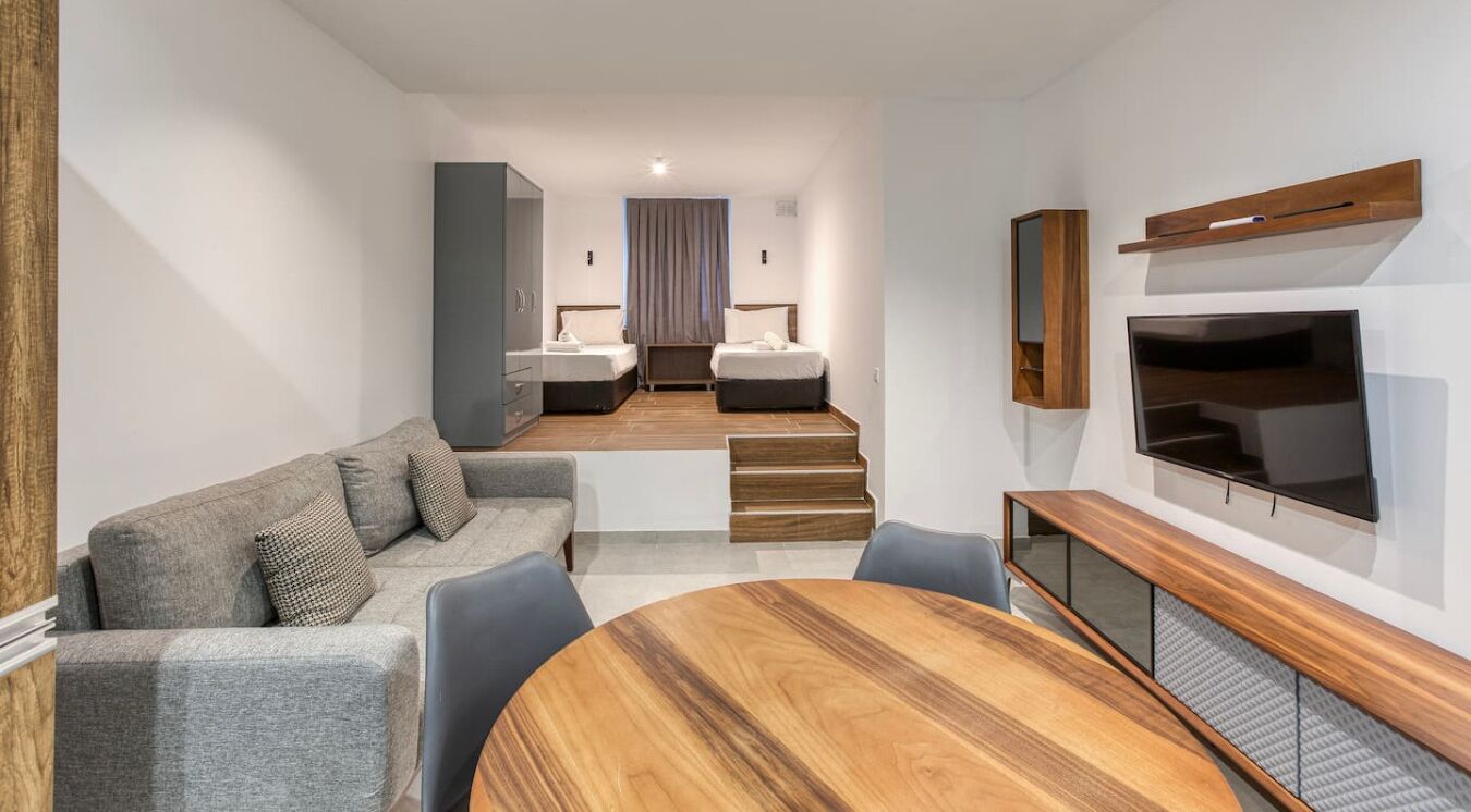 Una camera d'albergo moderna con un divano, un tavolo da pranzo, una TV e una scala che conduce a una zona notte.
