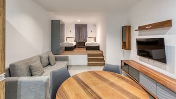 Una camera d'albergo moderna con un divano, un tavolo da pranzo, una TV e una scala che conduce a una zona notte.