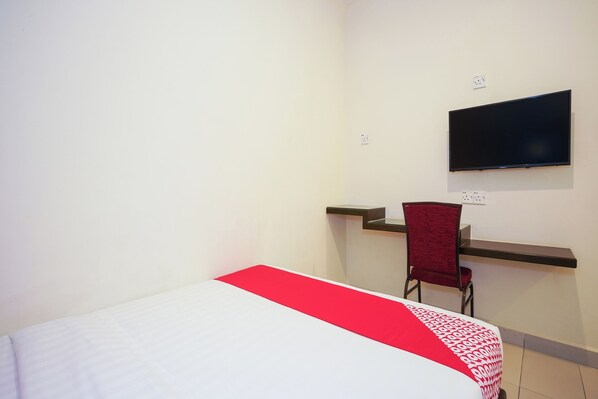 Une chambre d’hôtel équipée d’un lit, d’un bureau, d’une chaise et d’un téléviseur fixé au mur.