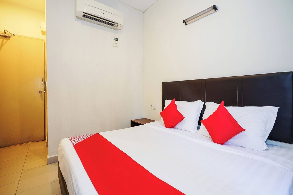 Une chambre d’hôtel avec un lit, une table de chevet, un climatiseur fixé au mur et une porte.